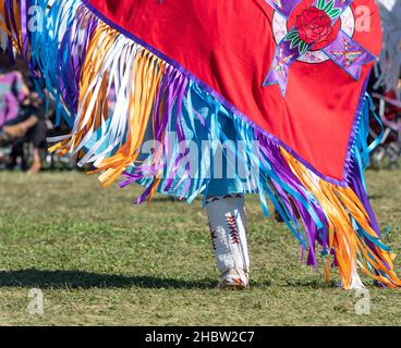 Gros plan sur les mocassins hauts de genou à perles blanches et le châle rouge décoré de rubans de satin colorés portés par une femme amérindienne dansant à un pow-wow Banque D'Images