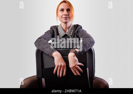 Femme d'affaires, jambes écartées, assise sur une chaise à l'envers, sur un fond gris Banque D'Images