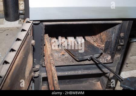 Nettoyage de la chaudière à combustible solide des restes de bois de chauffage et de charbon.Chaudière avec amortisseur ouvert.Efficacité de chauffage dans la maison. Banque D'Images