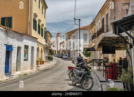 Leflimmi, Corfou, Grèce - 03 août 2021: Les gens visitent le bar local sur une vieille rue étroite typique avec le Saint Temple d'Agios Arsenios.Lefkimmi est le sou Banque D'Images