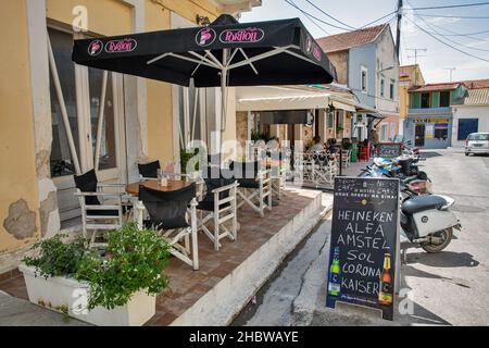 Leflimmi, Corfou, Grèce - 03 août 2021: Les gens visitent le bar local sur une vieille rue étroite typique avec le Saint Temple d'Agios Arsenios.Lefkimmi est le sou Banque D'Images