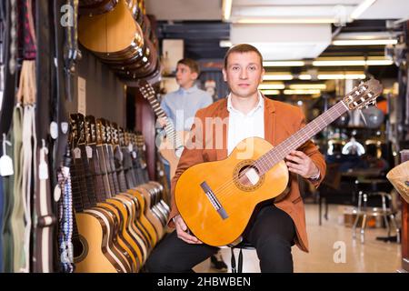 Joyeux vendeur de sexe masculin montrant de la guitare à un client de type garçon Banque D'Images