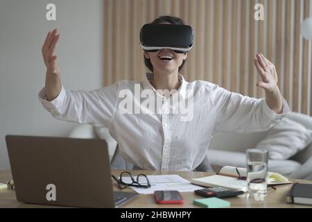 Une femme d'affaires européenne excitée teste les lunettes VR au travail Banque D'Images