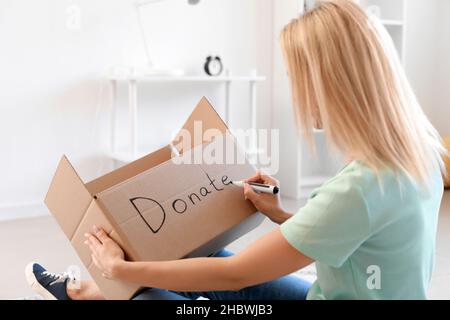 Jeune femme écrivant un don de mot sur une boîte en carton à la maison Banque D'Images