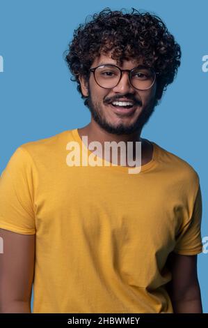 Joyeux jeune homme aux cheveux bouclés portant des lunettes élégantes Banque D'Images