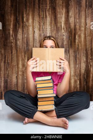 Adolescente assise avec une pile de livres et de peeking dehors de derrière le livre de texte sur un fond en bois Banque D'Images