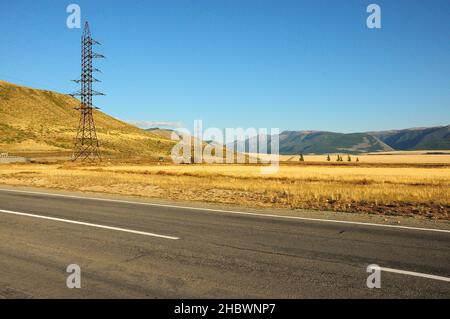 De grands poteaux métalliques de lignes électriques traversant la route traversent la steppe du désert.Kuraiskaya steppe, Altaï, Sibérie, Russie. Banque D'Images