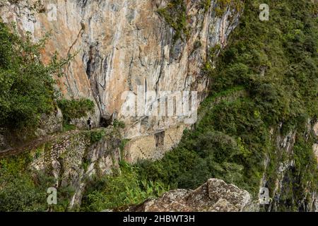 Une touriste femelle marche sur le chemin étroit vers une petite porte dans la montagne, Machu Picchu, Pérou Banque D'Images