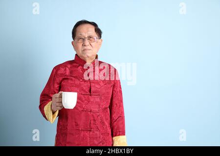 L'homme asiatique senior portant une chemise chinoise traditionnelle sur fond bleu. Banque D'Images