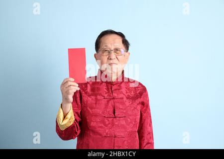 L'homme asiatique senior portant une chemise chinoise traditionnelle sur fond bleu. Banque D'Images