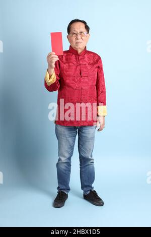 L'homme asiatique senior portant une chemise chinoise traditionnelle sur fond bleu. Banque D'Images