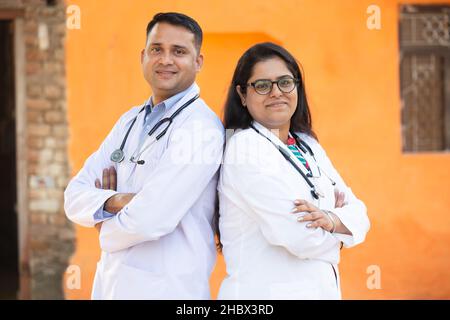 Portrait de jeune Indien souriant Homme et Femme Docteur portant Stethoscope Croix debout bras regardant la caméra avec des émotions positives contre l'orang Banque D'Images