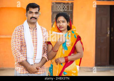 Portrait de jeune couple indien rural debout à l'extérieur à la maison de village.Moustache homme portant kurta et femme portant sari, mari femme portant tradi Banque D'Images