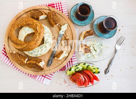 Bagel traditionnel turc, croustillant, simit au fromage crémeux, coupé en deux sur l'assiette en bois avec deux verres de thé. Banque D'Images