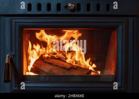 Foyer de cuisinière et bois brûlant derrière la porte de verre, coin de feu en métal noir, chaleur rayonnée de flamme, intérieur chaud, Banque D'Images