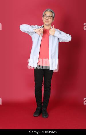 L'homme asiatique senior portant une chemise bleue avec de longs cheveux debout sur fond rouge. Banque D'Images