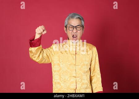 Le portrait d'un homme asiatique de premier plan portant un tradon chinois habillé debout sur fond rouge. Banque D'Images