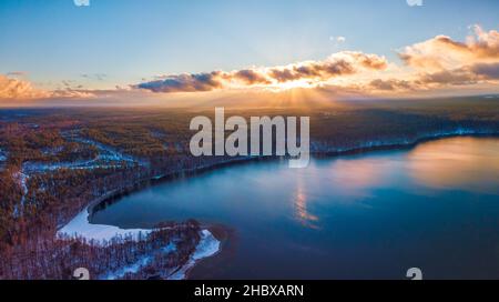 Vue aérienne du fond hivernal avec une forêt enneigée, un lac et des rayons de soleil sur le lac de Glukas en Lituanie Banque D'Images