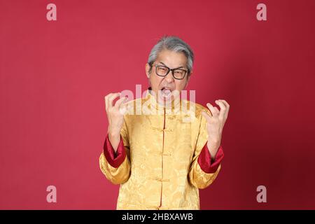 Le portrait d'un homme asiatique de premier plan portant un tradon chinois habillé debout sur fond rouge. Banque D'Images