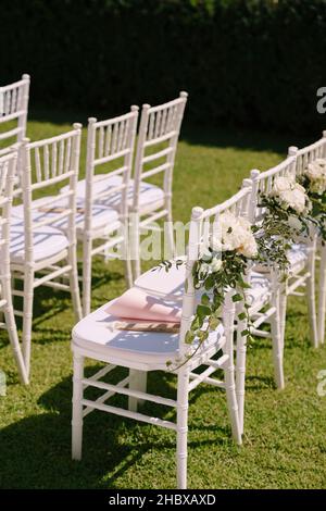 Une rangée de chaises blanches décorées de bouquets de fleurs se dresse sur une pelouse verte Banque D'Images