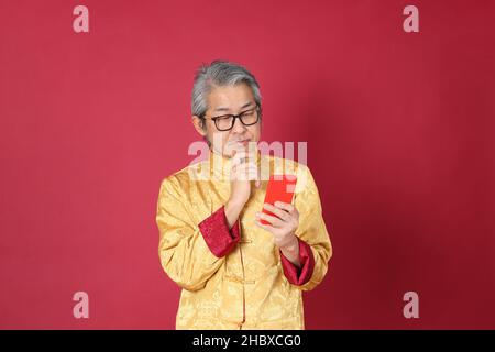 Le portrait d'un homme asiatique de premier plan portant un tradon chinois habillé debout sur fond rouge. Banque D'Images