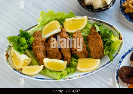 Détail tiré de la table de Ramadan, boulettes sans viande, cig kofte sur l'assiette ovale avec des feuilles de laitue et des tranches de citron. Banque D'Images