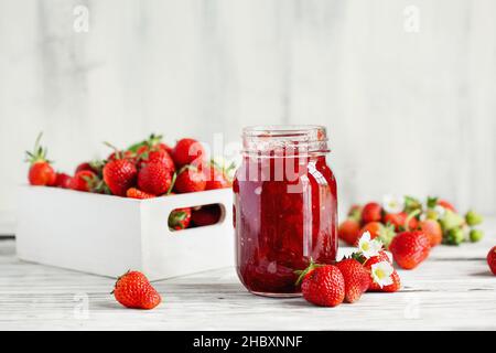 Conserves de fraises faites maison ou confiture dans un pot de maçon entouré de fraises fraîches bio. Mise au point sélective avec un premier plan et un arrière-plan flous. Banque D'Images