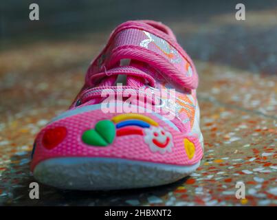 Photographie d'une petite profondeur de champ d'une chaussure décorative rose pour bébé sur un sol en béton poli. Banque D'Images