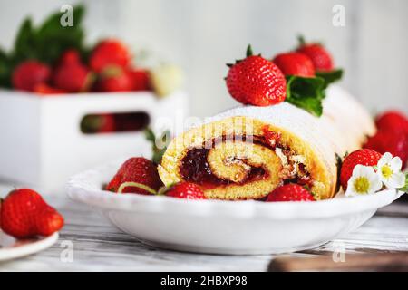 Roulades à gâteau sablé faits maison aux fraises ou roulade avec confiture de baies et sucre en poudre avec feuilles de menthe.Dessert sur une table rustique blanche. Banque D'Images