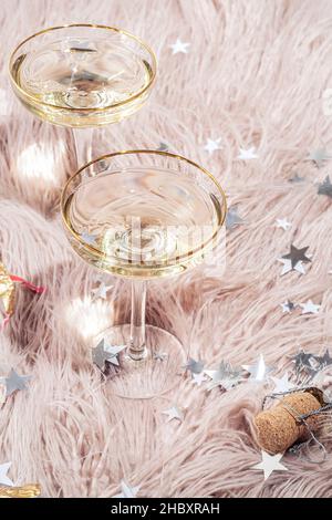 Deux verres de champagne sont debout sur un tapis en fausse fourrure rose avec des confettis dispersés autour.Le concept d'une fête, d'une nouvelle année ou de vacances. Banque D'Images