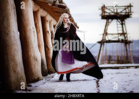 Magnifique viking blond habillé d'un manteau noir sur fond de château. Beau décor de film - un ancien village viking Banque D'Images