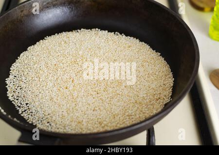 Le sésame est frit dans une poêle en fonte dans la cuisine.Le processus de préparation de la sauce Tahini traditionnelle.Concept de cuisine Levantine. Banque D'Images