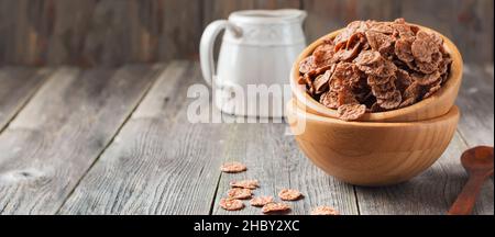 Cornflakes au chocolat pour le petit déjeuner dans une assiette de bambou sur fond de bois ancien.Flocons de maïs sains.Petit-déjeuner le matin.Bannière.Vue de dessus avec espace de copie. Banque D'Images