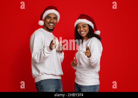 Joyeux amoureux du noir dans les chapeaux de père Noël pointant vers l'appareil photo Banque D'Images