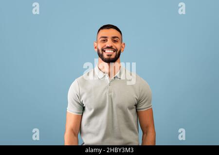 Portrait d'un homme arabe heureux souriant à l'appareil photo sur fond bleu studio, montrant des émotions positives Banque D'Images