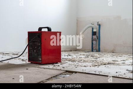 chauffage de ventilateur rouge sur un site de construction, résidus d'adhésif de carrelage et tuyaux d'évacuation en arrière-plan Banque D'Images