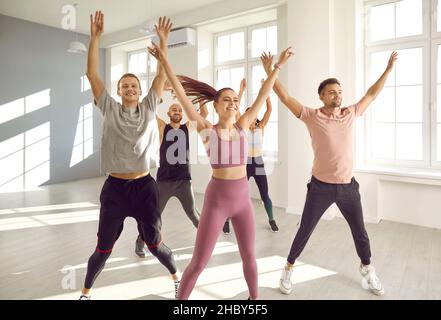 Groupe de jeunes heureux faisant des jacks de saut pendant un entraînement cardio à la salle de gym Banque D'Images