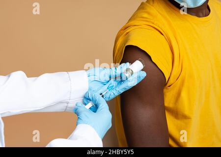 Médecin méconnaissable portant des gants médicaux bleus faisant la vaccination d'un patient masculin noir Banque D'Images