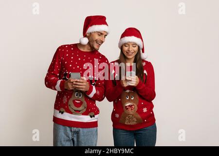 Joyeux jeune couple à Santa Hats jouant à Mobile Games sur les smartphones Banque D'Images