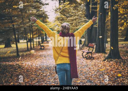 Bonne femme portant un chandail jaune, une écharpe rouge et un Jean.Parc public d'automne.Image en tons Banque D'Images
