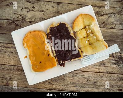 Ensemble de pain grillé avec différentes garnitures de beurre d'arachide, de chocolat et de beurre. Banque D'Images