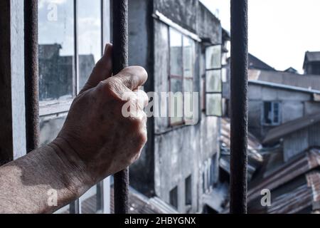 Main d’un homme asiatique âgé tenant un poteau de fenêtre en fer.Concept de solitude des personnes âgées, isolement social et traumatisme mental. Banque D'Images