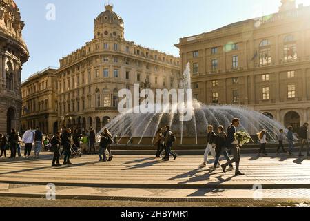 Vue à contre-jour de la Piazza de Ferrari avec des personnes marchant près de la fontaine et des rayons du soleil dans un jour ensoleillé d'automne, Gênes, Ligurie, Italie Banque D'Images