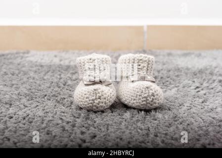 Chaussons bébé tricotés gris sur la moquette de la chambre.Vue avant Banque D'Images