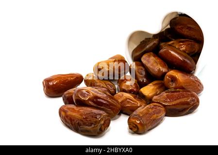 Les dates sont isolées.Les dates se déversent d'une tasse en forme de coeur sur un fond blanc gros plan.Fruits secs Banque D'Images