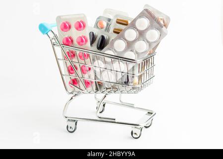 Beaucoup de pilules de médecine, des comprimés et des vitamines dans un petit panier de supermarché isolé sur fond blanc, photo pharmaceutique prise avec soft FO Banque D'Images