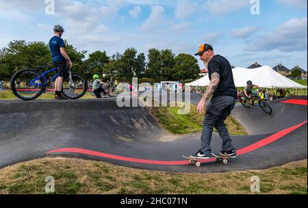 Enfants à vélo et homme à bord d'un skateboard lors d'un événement d'ouverture sur le circuit de pompe Ormiston BMX, East Lothian, Écosse, Royaume-Uni Banque D'Images