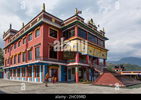 Un jeune moine bouddhiste à cheval en face du bâtiment principal du monastère Pema Tsal Sakya près de Pokhara, au Népal.Deux jeunes garçons suivent. Banque D'Images