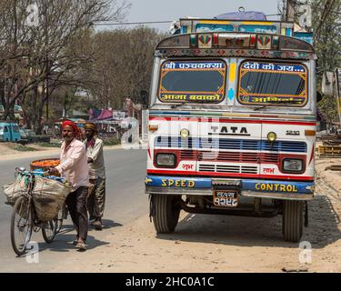 Deux vendeurs de rue marchent à côté d'un camion de transport de marchandises lourdes poussant des bicyclettes chargées de fruits pour la vente à Katmandou, Népal. Banque D'Images