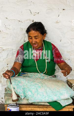 Une ancienne réfugiée tibétaine transforme la laine en fils à la main pour faire des tapis dans un village de réfugiés de Pokhara, au Népal. Banque D'Images